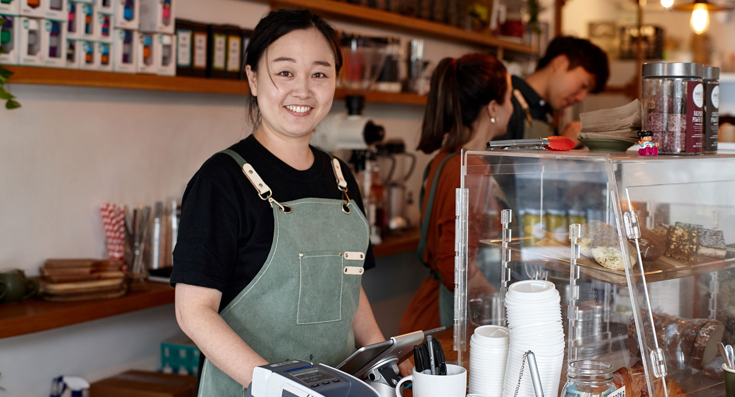 Shop owner smiling whilst working inside coffee shop.