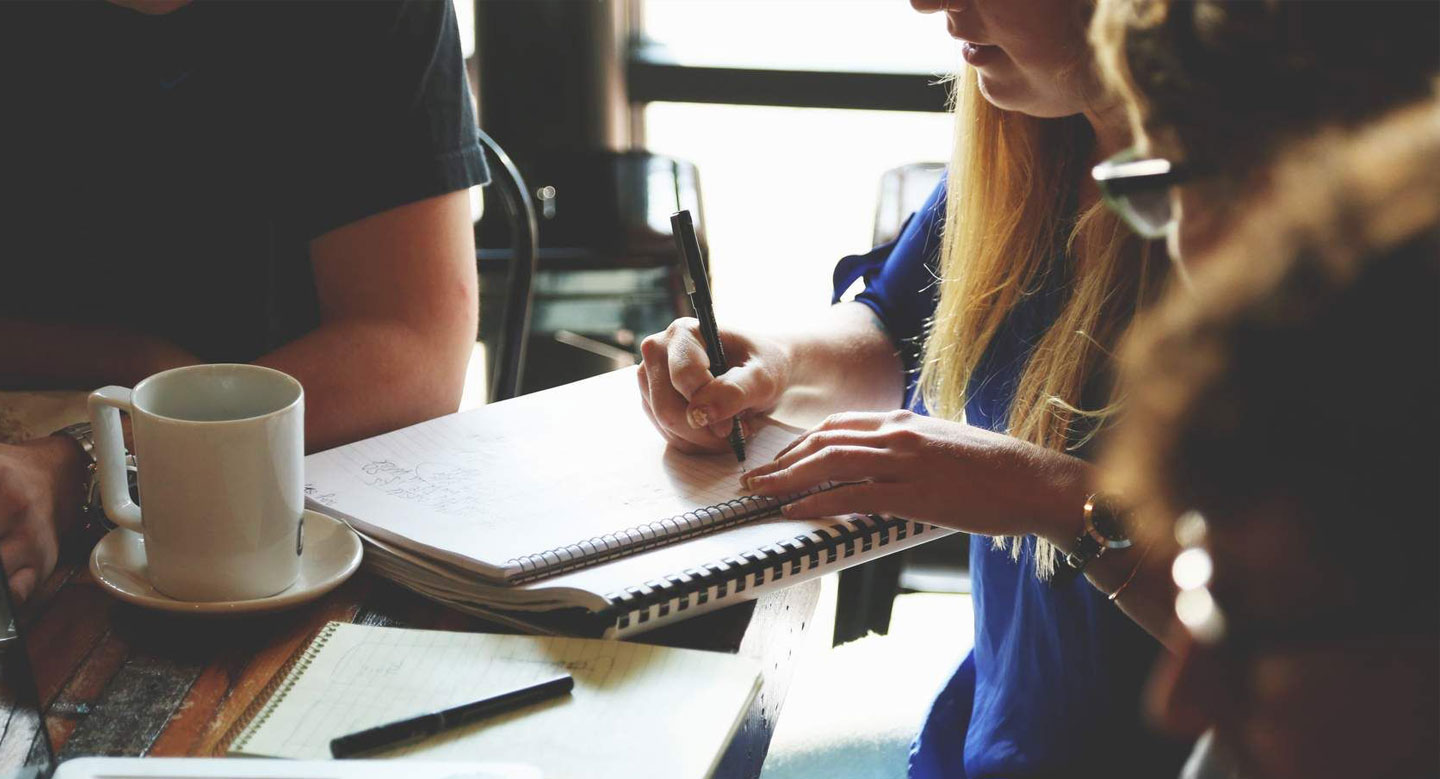 A group of people sitting around a wooden table contributing to writing a report