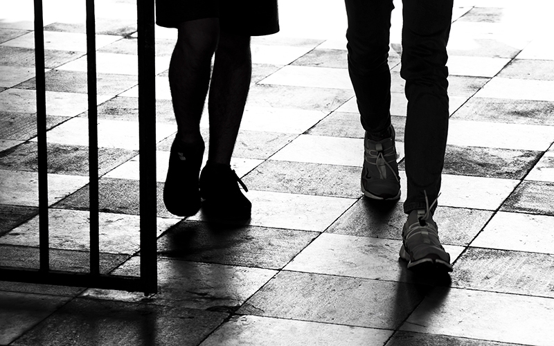 silhouette of two people walking through a barred gate