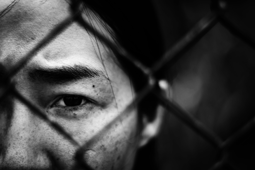 A sad woman looking this a chain-link fence.