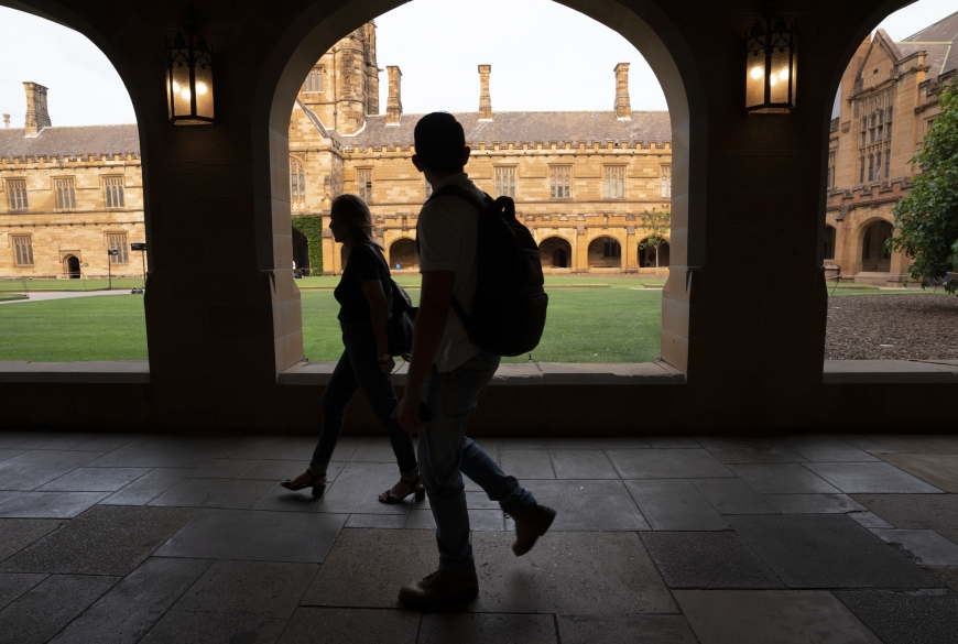 Image of shadowed university students walking through open corridor alongside university quadrangle