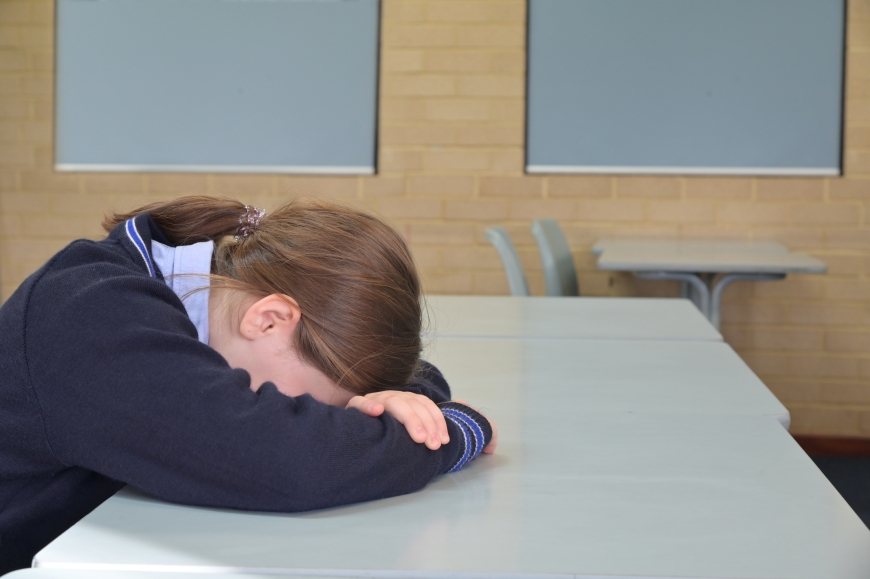 School girl sitting at desk with head in hands.