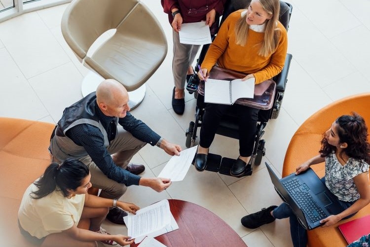 Group of people sitting around a table holding paper and laptops and discussing something 