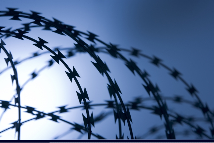 barbed wire at the top of a fence at a jail under the bright blue sky of a warm day