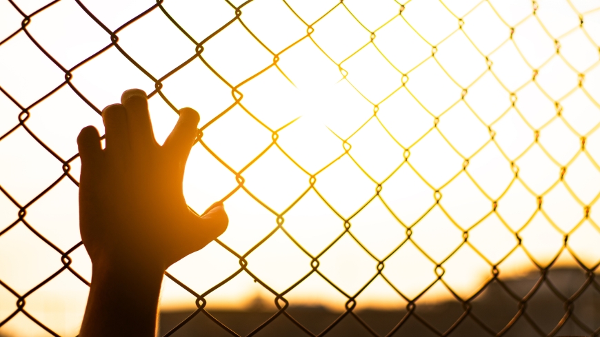 Young hand holds fence as sun sets in distance