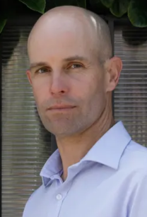 headshot of man with bald head wearing blue shirt