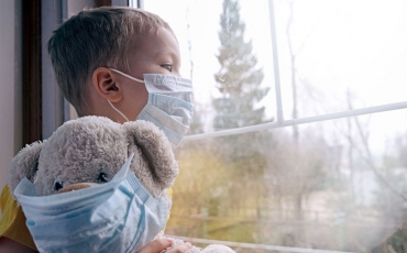 Sad child in quarantine with mask and masked teddy bear