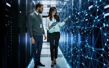 Two people stand in a hallway surrounded by computers