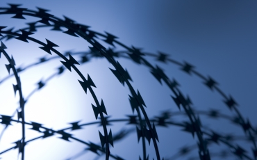 barbed wire at the top of a fence at a jail under the bright blue sky of a warm day