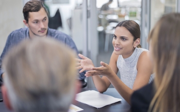 A young woman and man at work among a group of people sitting an office.