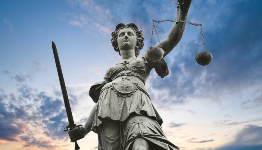 Outdoor metal statue of Justice with sky in background.