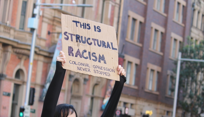 Protester holding up sign at Black Lives Matter March in Sydney 2020. Sign reading 'This is structural racism, colonial oppression never stopped'.