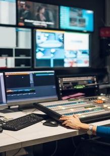 Middle aged woman in blue shirt sitting at a desk using equipment in control room on a TV station