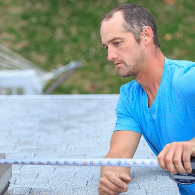 A Caucasian man  is using a measuring tape on a construction site. He is wearing hearing aids.