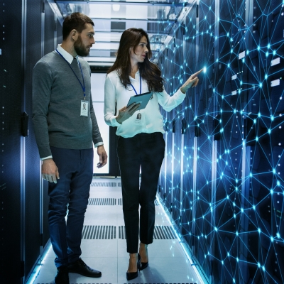 Two people stand in a hallway surrounded by computers