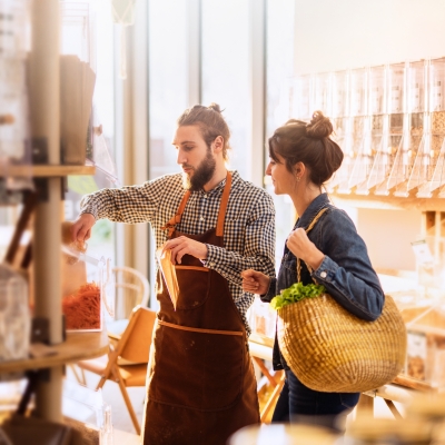 A wide shot of a supermarket store worker assisting a customer with purchasing herbs.