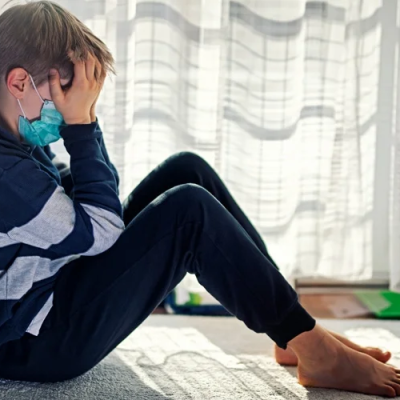 Child wearing a facemask sitting with head in hands